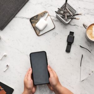 Overhead view of a stylish desk with smartphone, coffee, and office supplies on marble surface.